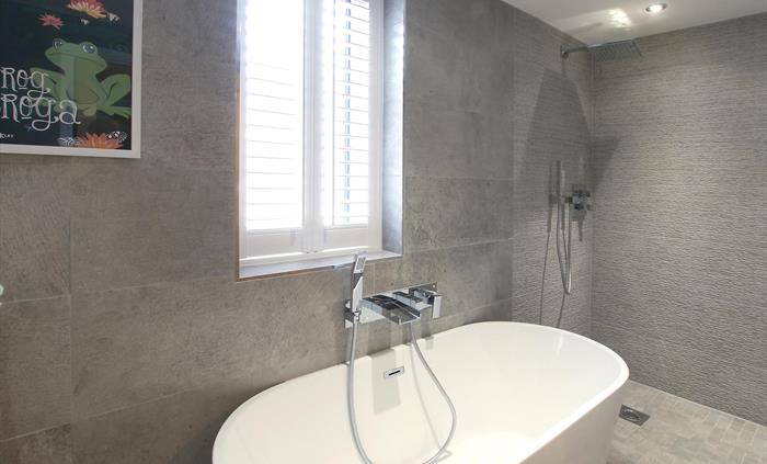 Sophisticated bathroom with textured grey tiles, a large freestanding bathtub, and a walk-in rainfall shower.